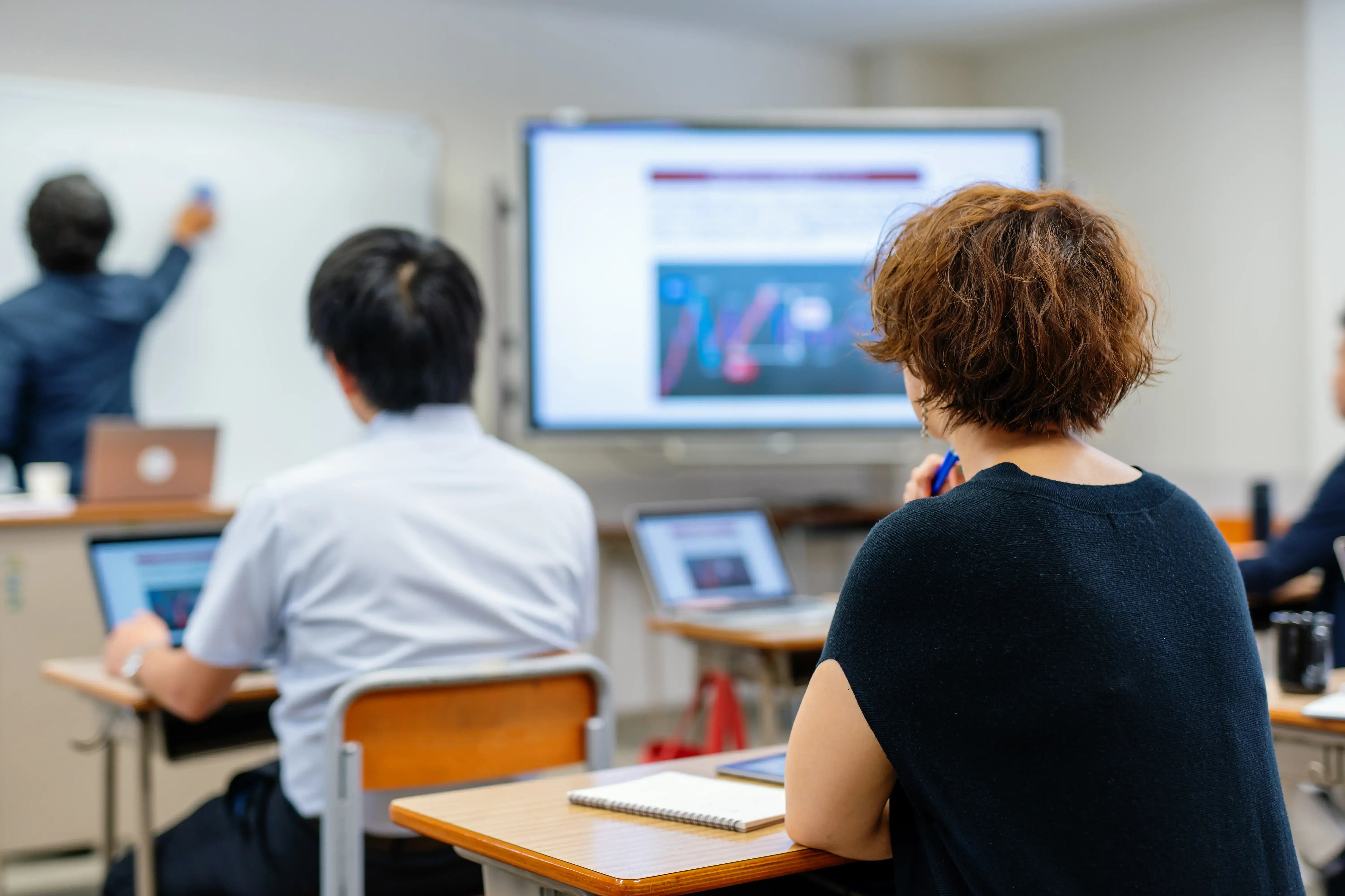 A teacher uses educational technology to support visual learning for students watching a display screen as the teacher clicks through with a remote