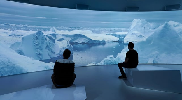 Two figures watching an immersive experience are silhouetted against a 4K projector screen showing an ocean ice field.