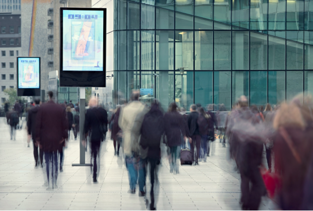A crowd on a modern city street walks past a number of digital displays showing crisp imagery on outdoor screens.