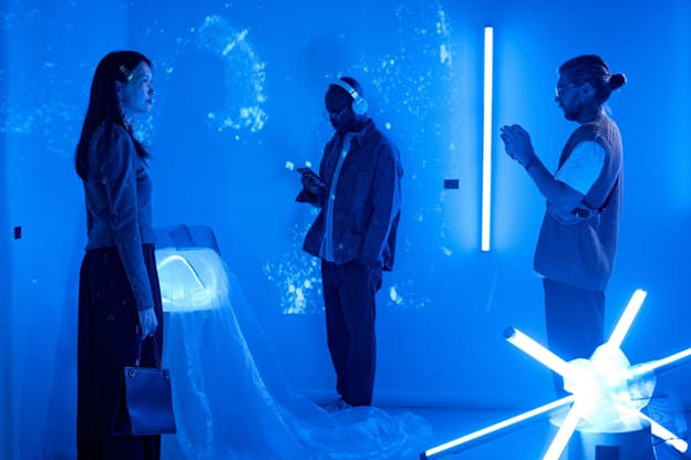 Three people move through an immersive experience in a blue room with projections on the wall and abstract lights.