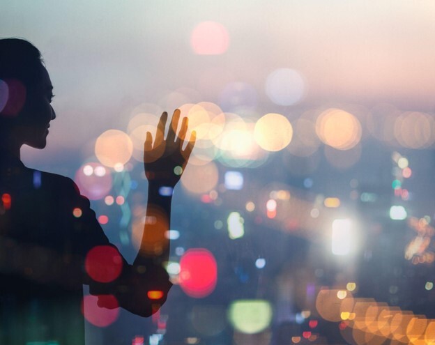 A woman's silhouette stands before the lights of an abstract projection mapping display created by DLP projectors.
