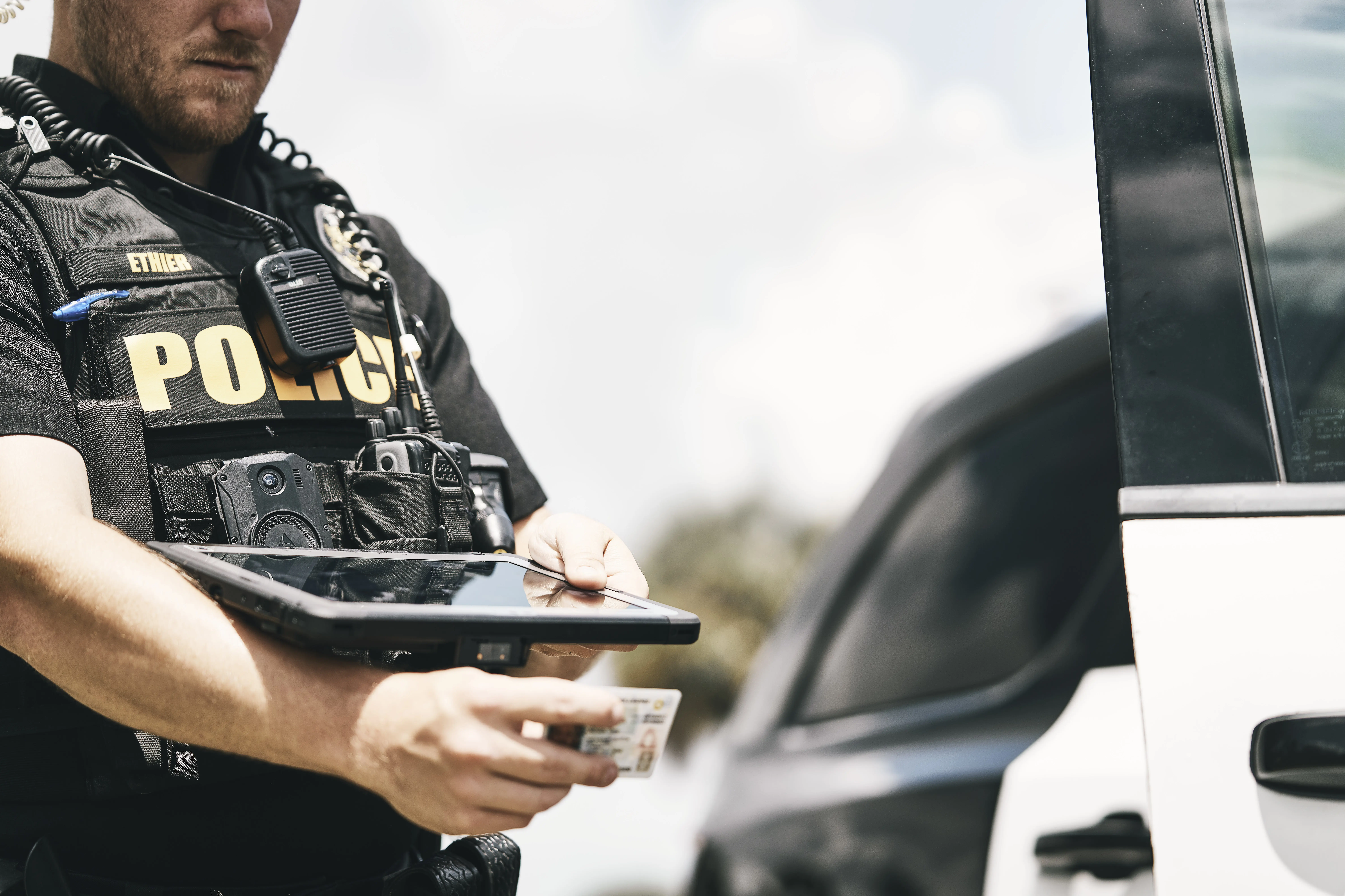 A law enforcement officer uses police technology to scan a driver's license on the side of the road.