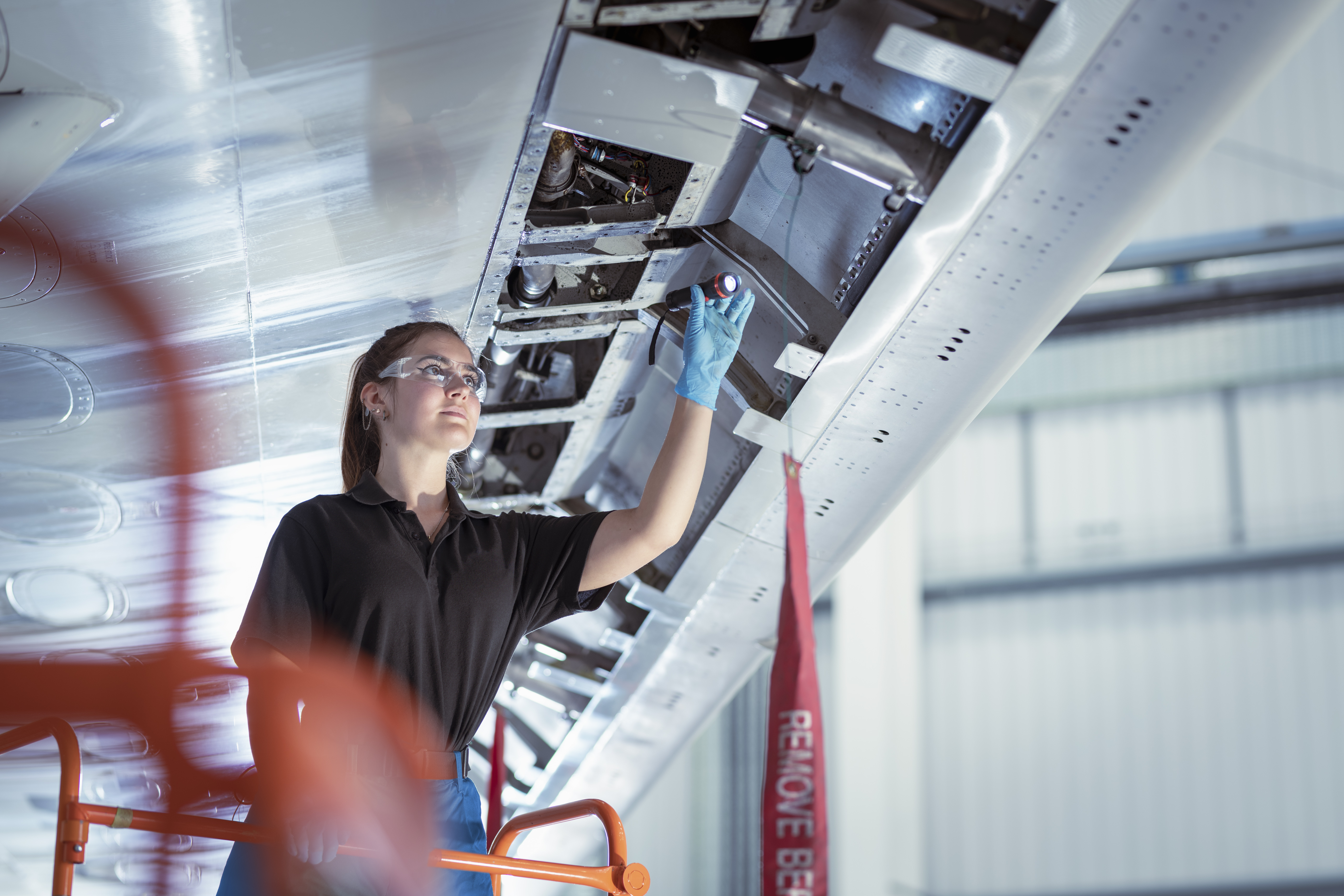 Female apprentice aircraft maintenance engineer inspecting airplane wing