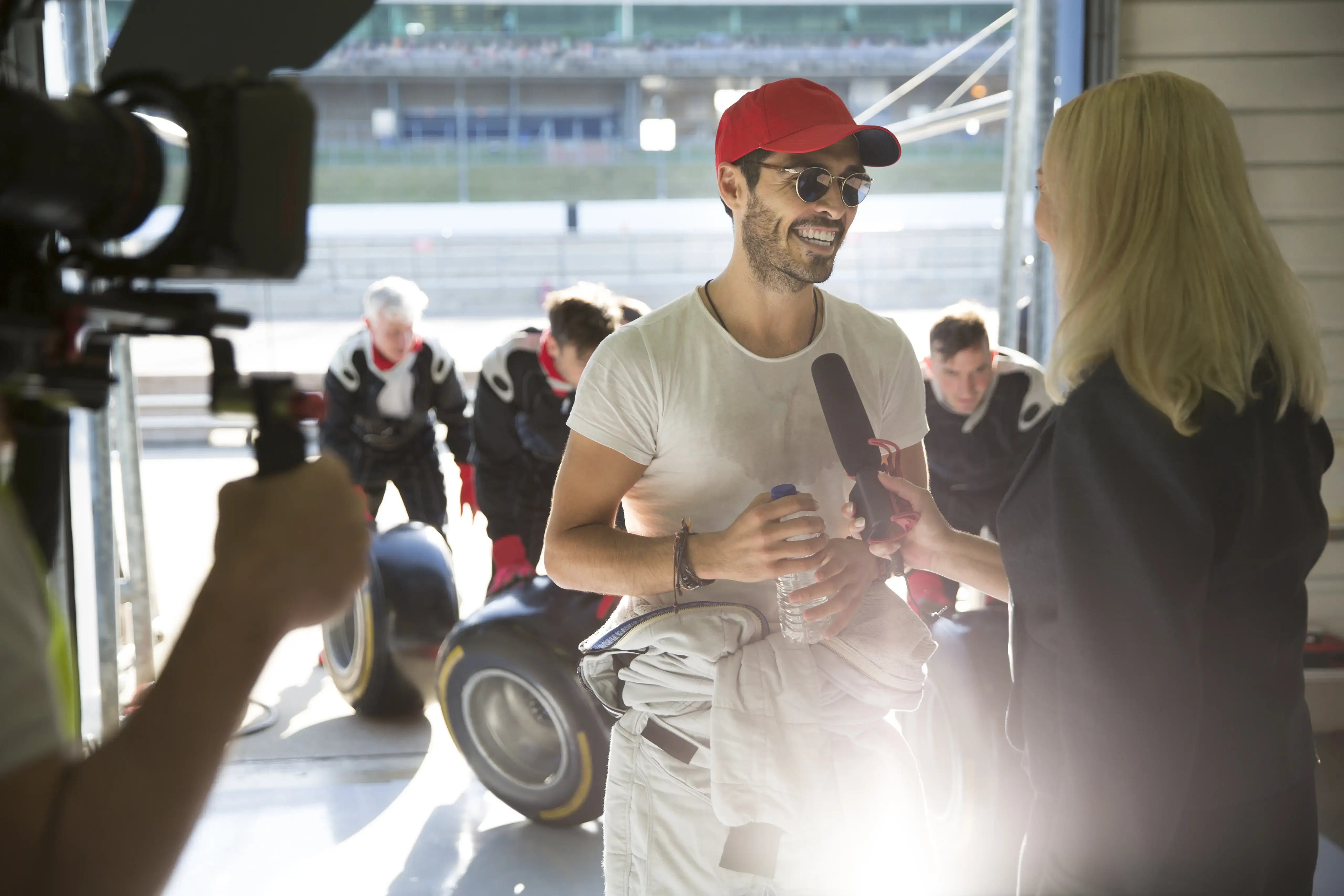 Female news reporter interviewing male open-wheel single-seater racing car race car driver in repair garage