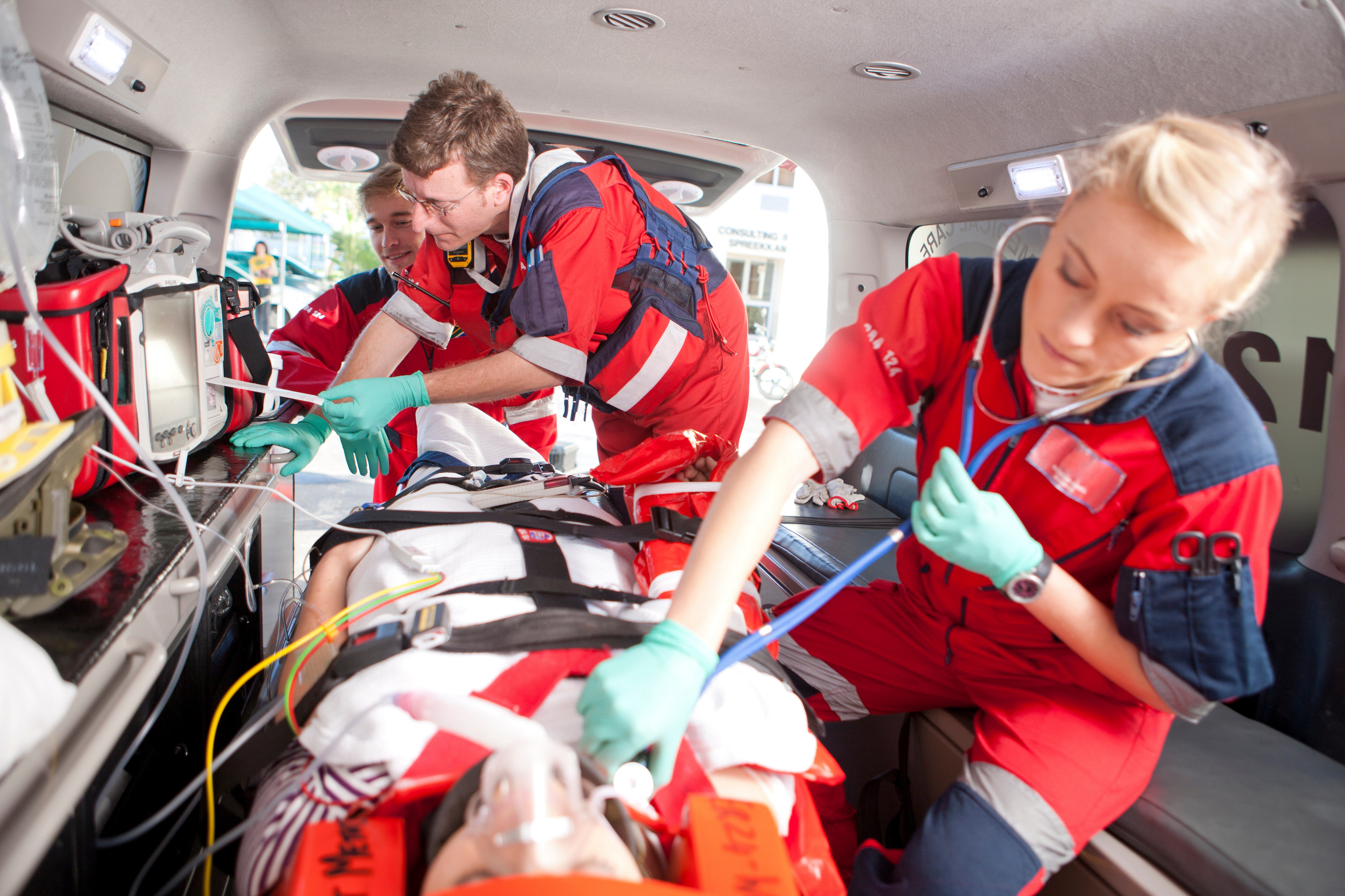 Paramedics using stethoscope on patient in ambulance