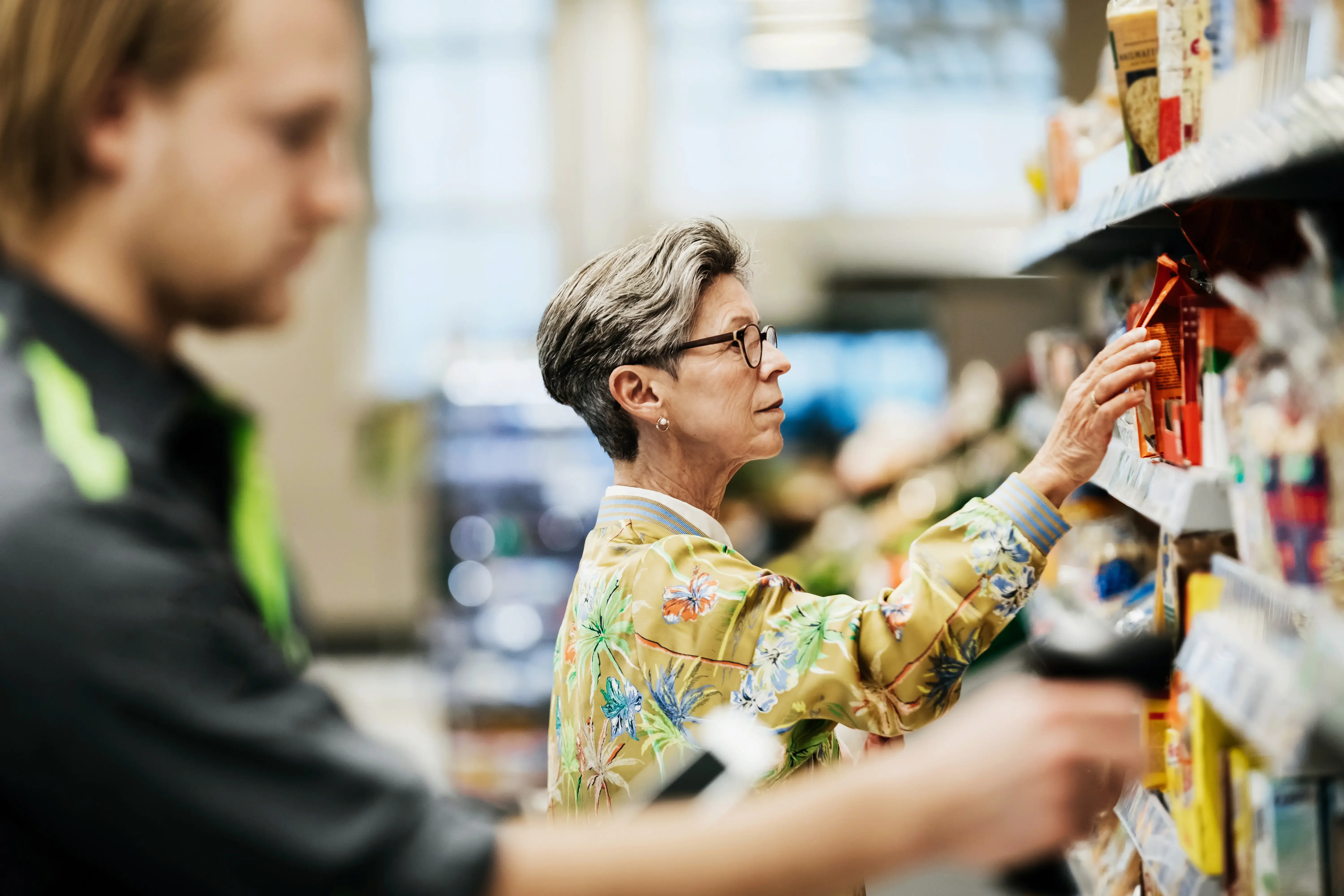 Senior Woman Picking Goods From Shelf At Supermarket