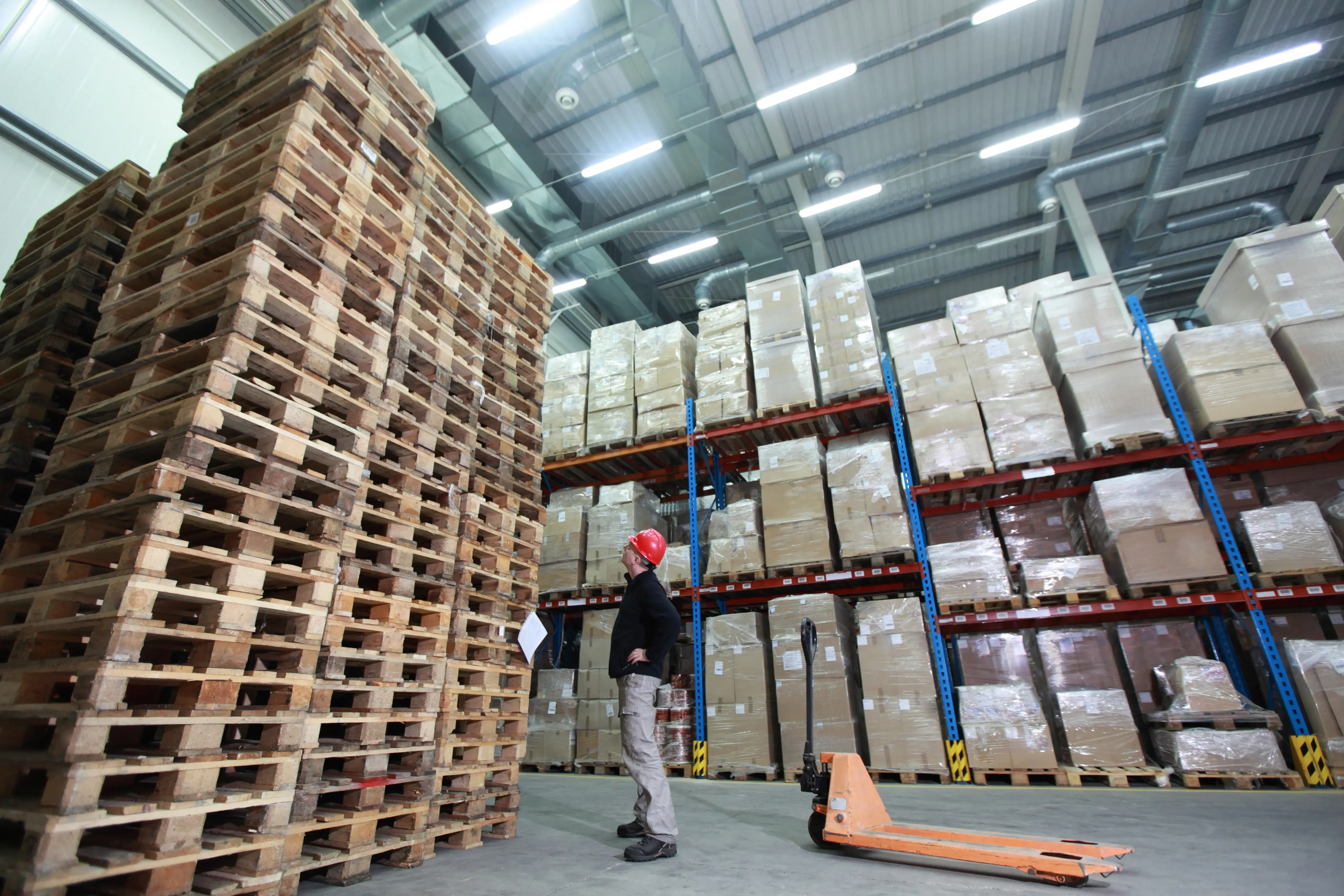 worker,hand pallet truck, stack of wooden pallets in storehouse